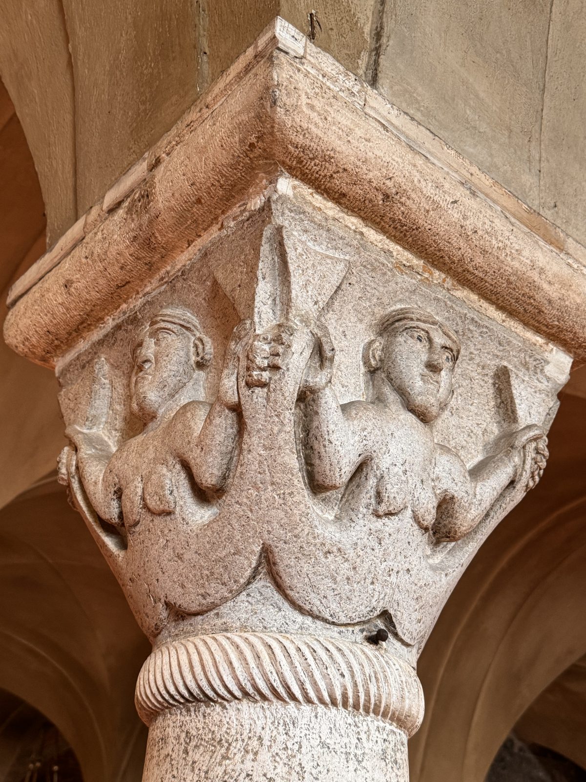 A crypt capital with two figures among leaves, carved with the soft, rounded forms typical of Wiligelmo’s workshop