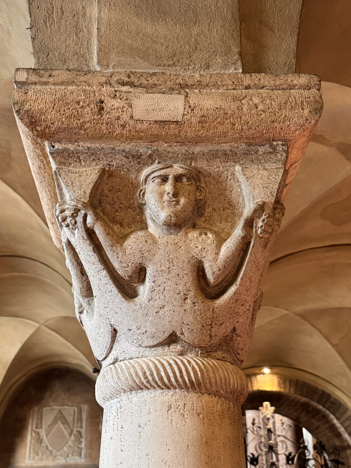 A frontal figure with raised arms, between prayer and the gesture of the sirens holding their tails