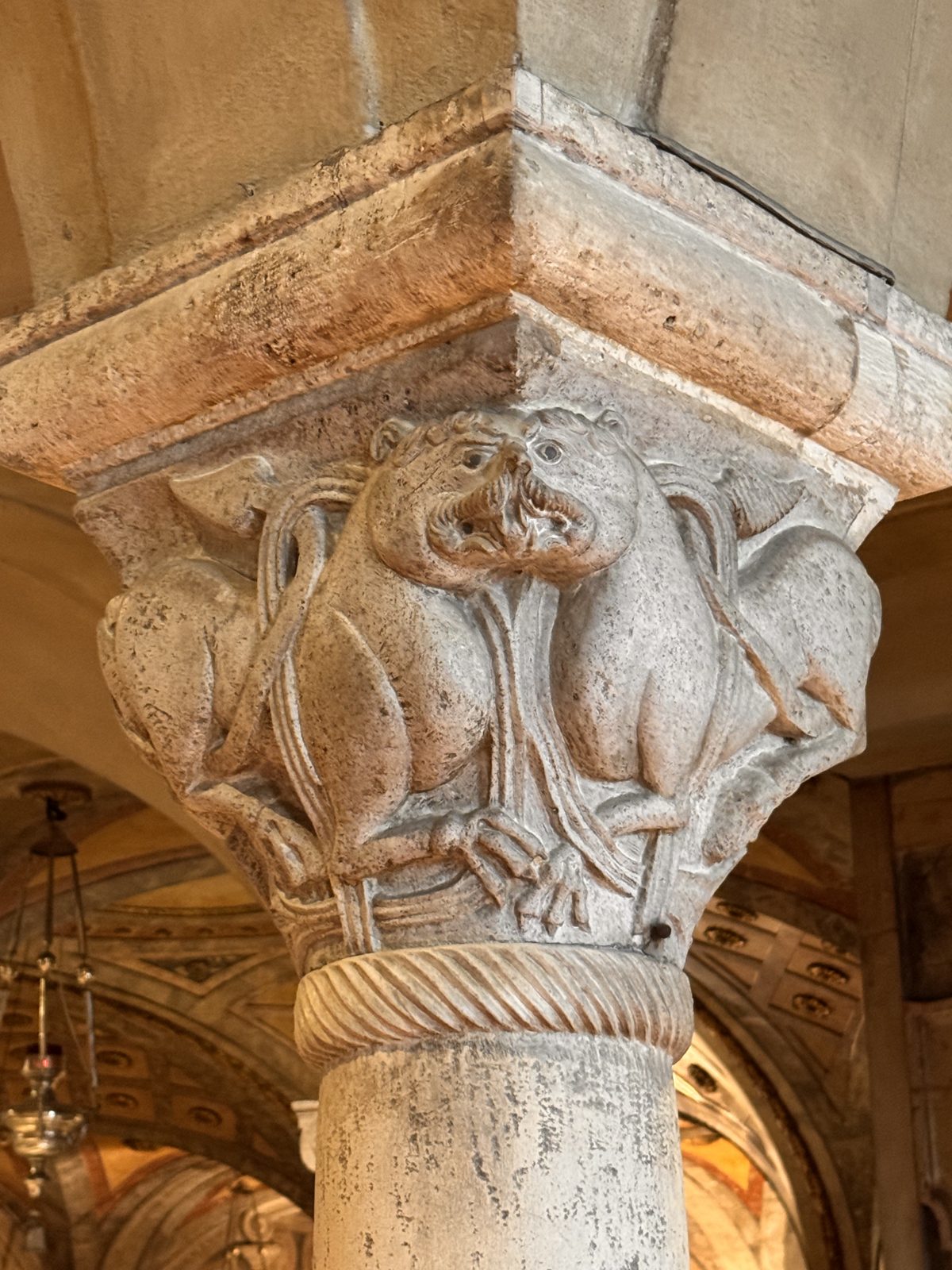 Two lions sharing a single head at the corner of the capital, a device that turns the beasts into guardians of the column