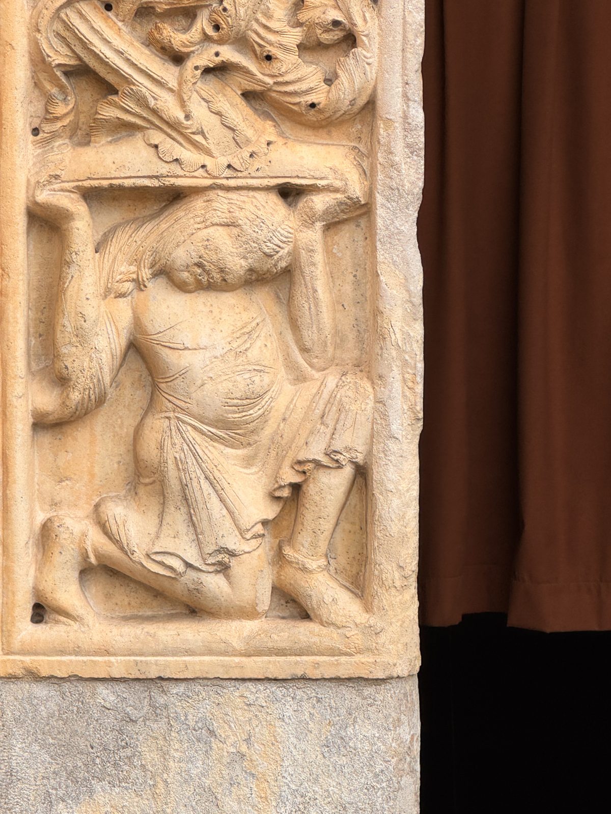 A crouching figure straining under the weight of the foliage above: an image of human labour and of the burden of sin